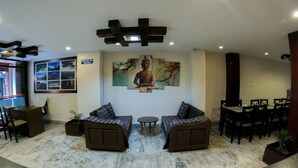A lobby with a Buddha statue, two sofas, a small round table, and a check-out time sign. - Hotel Royal Mantra (Kathmandu)