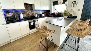 A modern kitchen with white cabinets, a built-in oven, a microwave, and a large island with bar stools. - Stunning Sea View Two Bed Apartment - With Balcony (Southbourne)