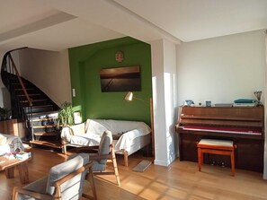 A living room with a green accent wall, a piano, a staircase, and a sofa.