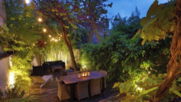 Un espace de restauration en plein air, avec une table et des chaises, entouré d’une végétation luxuriante et illuminé de guirlandes lumineuses.