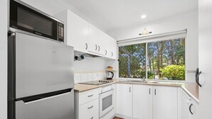 Una cocina moderna con armarios blancos, un refrigerador de acero inoxidable, un microondas, un horno y un lavaplatos.