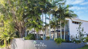 Un resort rodeado de palmeras y follaje, con un cartel que indica 'Tropical Palms Resort'.