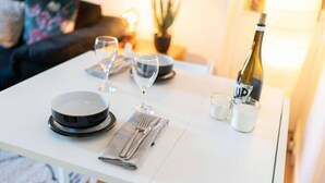 Ruokapöytä on katettu lautasilla, laseilla, pullolla ja pienellä kannulla. Taustalla näkyy sohva ja kasvi.