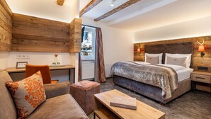 A cozy bedroom with a large bed, a wooden headboard, a nightstand, a desk with a chair, and a view of the outside. - Hotel Zehnerkar & Hotel Obertauern (Tweng)