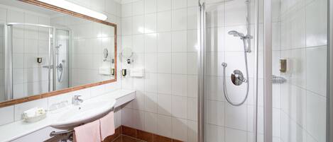 Un baño moderno con ducha envuelta en vidrio, un lavabo blanco y un espejo grande.
