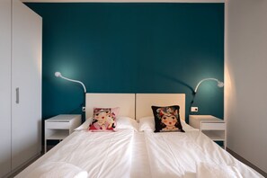A double bed with white bedding, two decorative pillows, and a teal accent wall.
