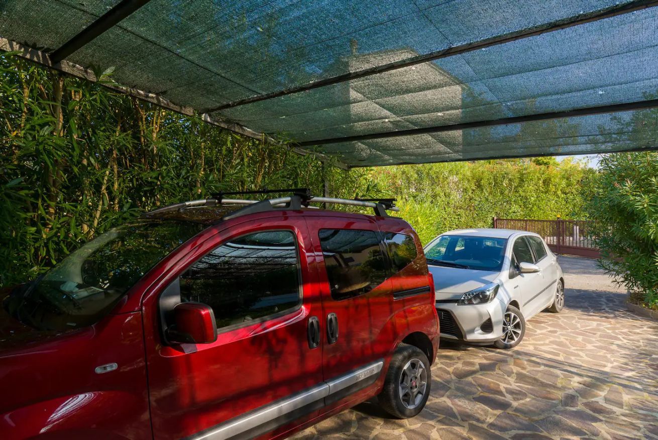 A red car parked under a covered area with a stone floor.