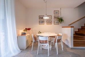 A dining area with a round table, white chairs, and a small side table with books and a lamp.