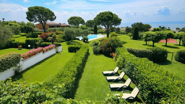 Un jardin magnifiquement entretenu, avec une piscine, des chaises longues et une vue sur la mer.