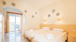 Une chambre d’hôtel avec deux lits, une petite table de chevet, une armoire et un balcon avec des rideaux.