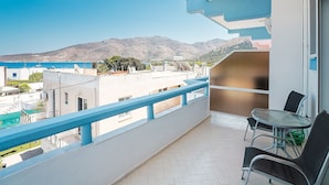 Un balcon avec vue sur la mer et les montagnes, une table avec des chaises et un petit espace jardin.