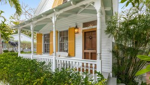 A white house with yellow shutters, a porch with a white railing, and a number "1112" on the door. - BRIGHT SUNSHINY DAY ~ Renovated 3 BR, 4 Ba Home w/ Pool, Spa & Exercise Room! (Key West)