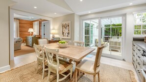 A dining area with a wooden table and chairs, a bowl of fruit, and a view of the outdoors through large sliding glass doors. - BRIGHT SUNSHINY DAY ~ Renovated 3 BR, 4 Ba Home w/ Pool, Spa & Exercise Room! (Key West)