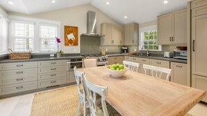 A modern kitchen with beige cabinets, a wooden dining table, and a large window with blinds. - BRIGHT SUNSHINY DAY ~ Renovated 3 BR, 4 Ba Home w/ Pool, Spa & Exercise Room! (Key West)