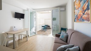 A modern living room with a flat-screen TV, a sofa, a dining table with chairs, and a glass door leading to a balcony. - Apartment "Dimora Idrusa" with Parking, Private Terrace, WiFi and Air Conditioning (Otranto)