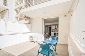 A modern apartment with a balcony, a dining area with blue chairs, and a kitchen visible through an open door.