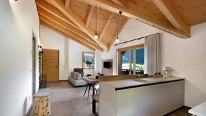 Une cuisine moderne dotée d’un grand îlot central, de poutres en bois au plafond et offrant une vue sur les montagnes par la fenêtre.