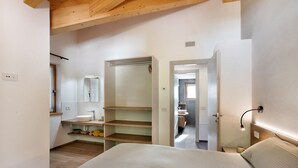 Une chambre à coucher comprenant un lit, une table de chevet, une commode, un miroir, une armoire et une salle de bain visible à travers une porte ouverte.