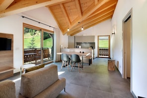A modern kitchen with a dining area, large windows, and a wooden ceiling.