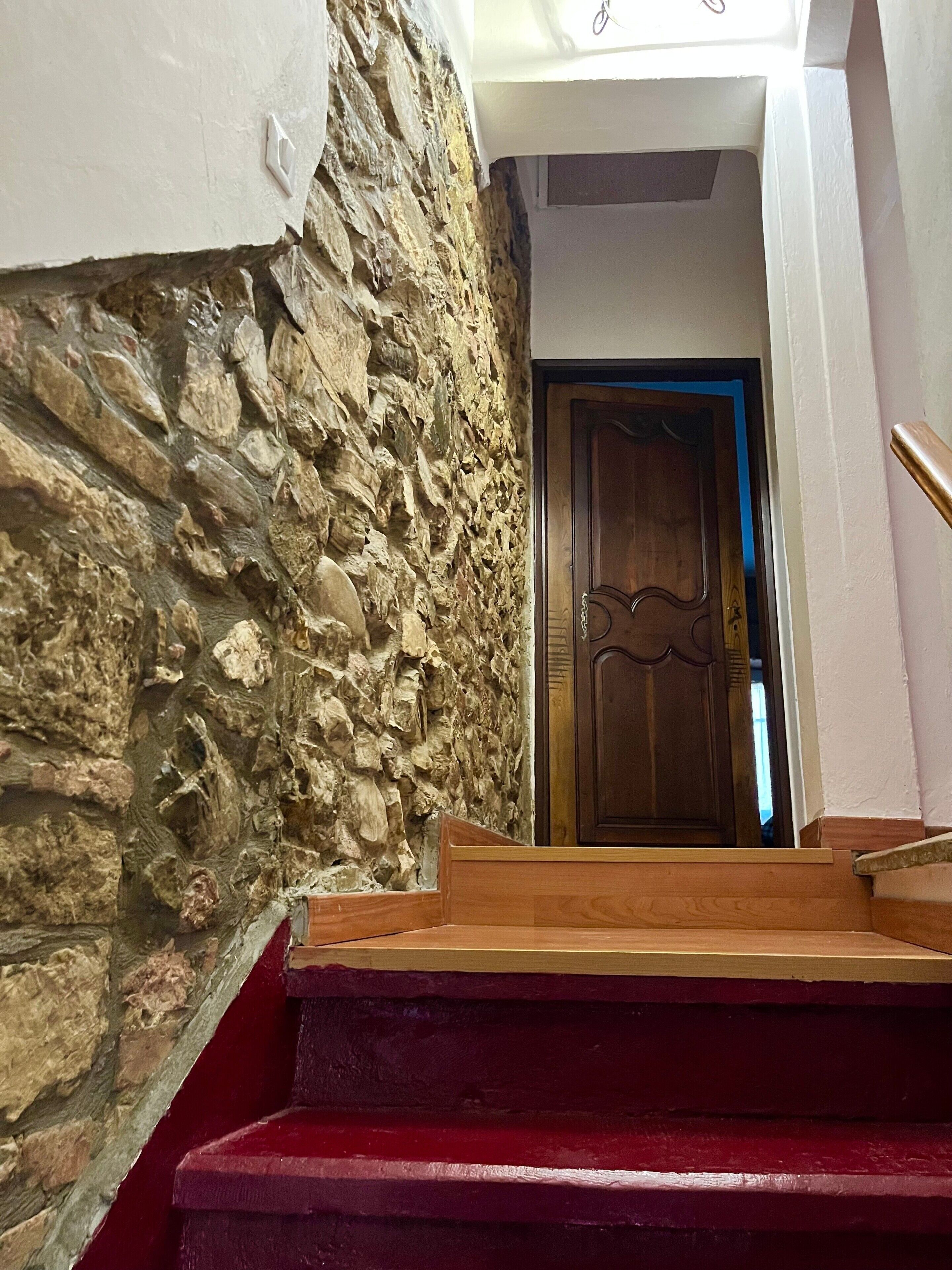 Un escalier avec un mur en pierre d’un côté et une porte en bois en haut.