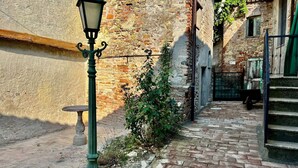 Une ruelle étroite pavée de pierres, avec un lampadaire ancien, un mur de briques et un escalier menant à un immeuble.