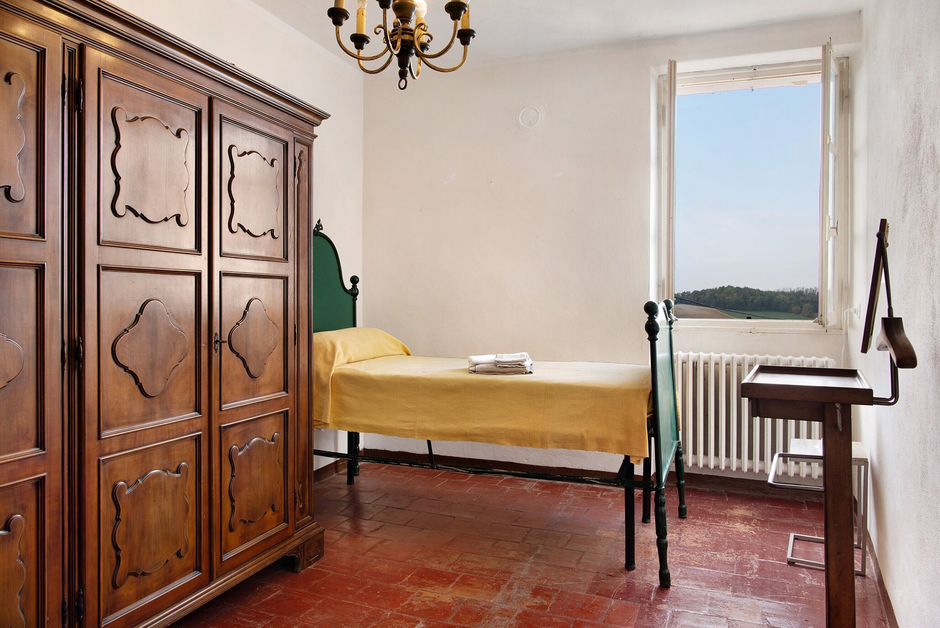 A room with a bed, a wooden cabinet, a radiator, and a window with a view.