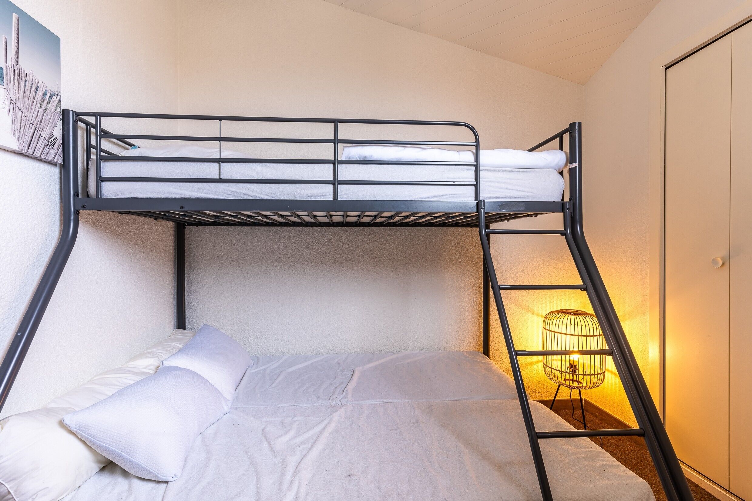A bunk bed with white bedding, a ladder, and a wall-mounted light fixture.