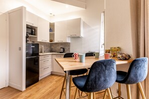 Una cocina compacta con electrodomésticos modernos, una mesa de comedor con sillas y un refrigerador pequeño.