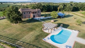 Una casa de piedra con piscina, rodeada de césped y árboles.