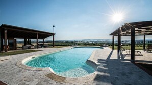 Una piscina con una pérgola y zona de descanso, rodeada por un patio de ladrillo.