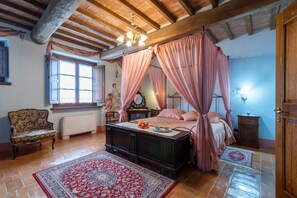 A bedroom with a four-poster bed, a wooden bench, a radiator, a window, and a door.