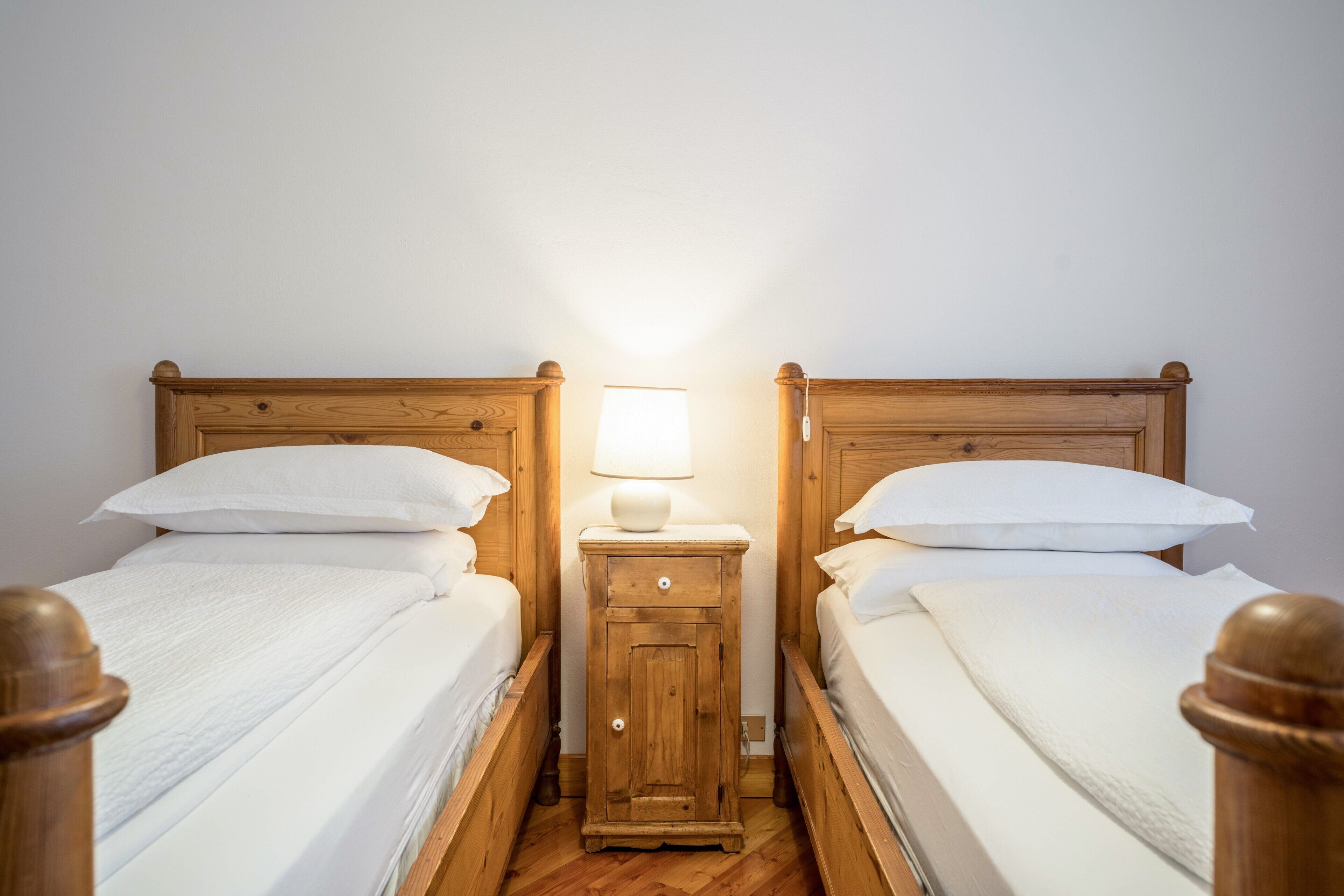 Ein Zimmer mit zwei hölzernen Betten, jeweils mit weißer Bettwäsche und einem Nachttisch mit Lampe dazwischen.