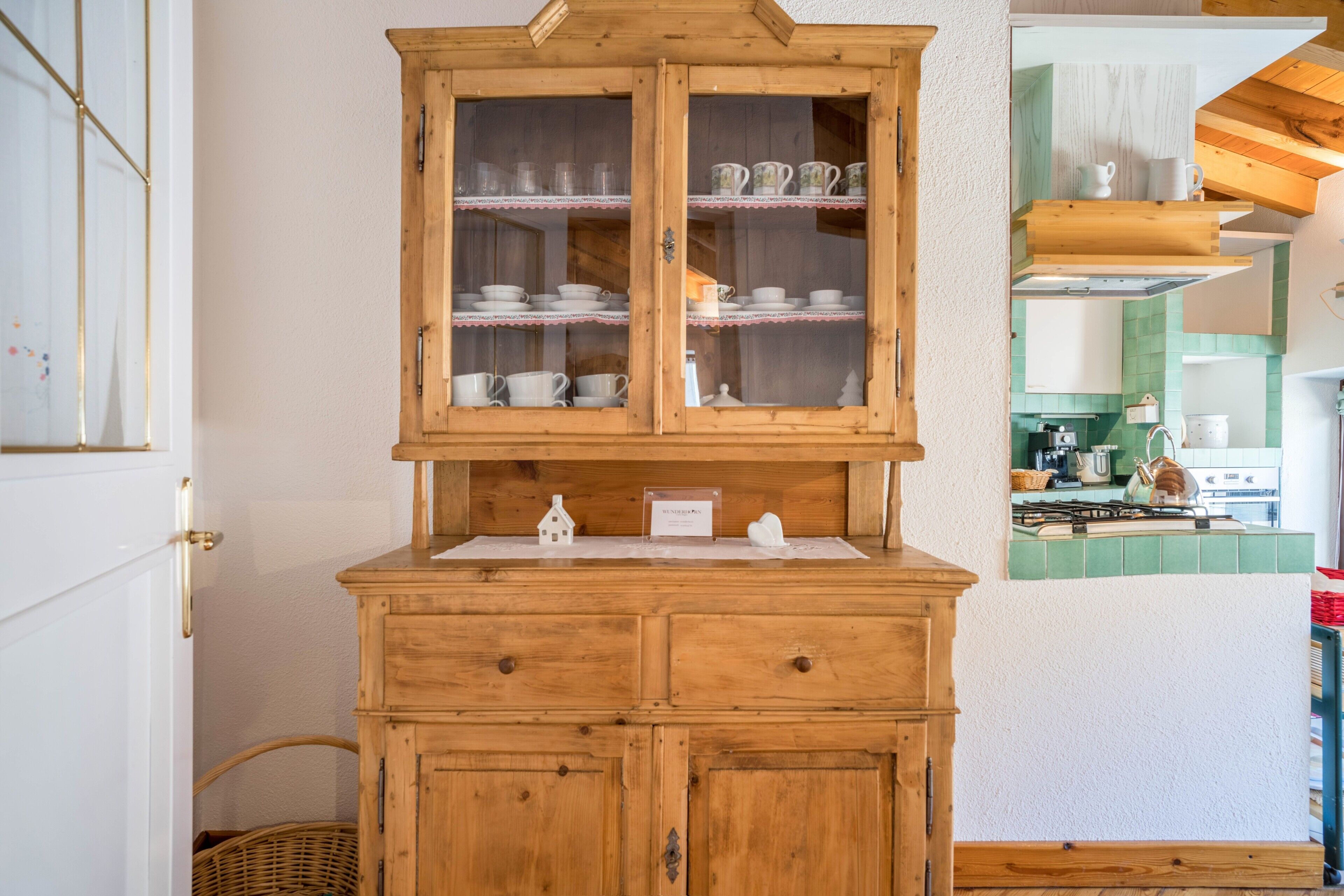 Un mobile in legno con vetrine che contiene piatti bianchi e un piccolo modellino di casa sullo scaffale.