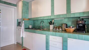 Una cocina con baldosas verde mar, armarios blancos, una cafetera y un tostador.