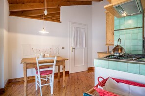 A kitchen with a wooden table, white chairs, a red basket, and a stove. - Wunderhorn Holiday Home with Private Terrace and Wi-Fi (Civezzano)