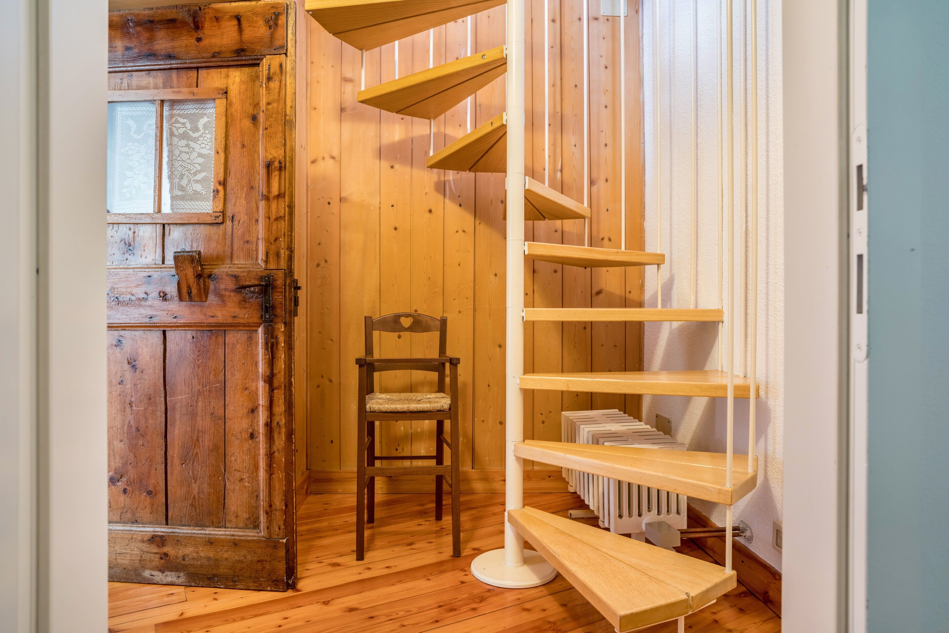 Un intérieur en bois avec un escalier en colimaçon, une chaise et une porte.