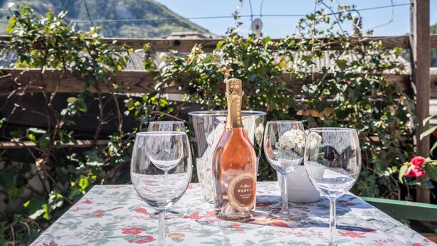 A table with a bottle of champagne, empty wine glasses, and a floral tablecloth. - Wunderhorn Holiday Home with Private Terrace and Wi-Fi (Civezzano)