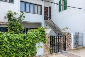 A white building with a stone staircase, a metal gate, and a hedge.