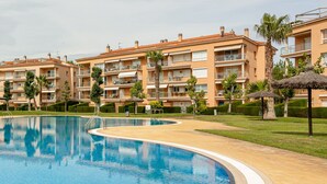 Piscina rodeada por edifícios de apartamentos com varandas, palmeiras e céu claro.
