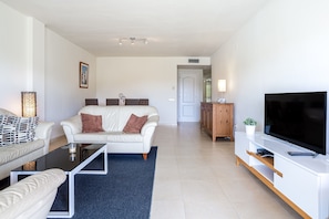 A modern living room with a white sofa, a coffee table, and a TV on a white stand.