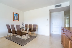 A dining area with a glass table and six chairs, a wooden cabinet, and a door leading to another room.