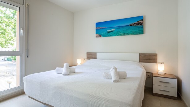 Quarto de hotel com uma cama grande, duas mesas de cabeceira, um criado-mudo, um quadro de uma paisagem costeira e uma janela com vista para o exterior.