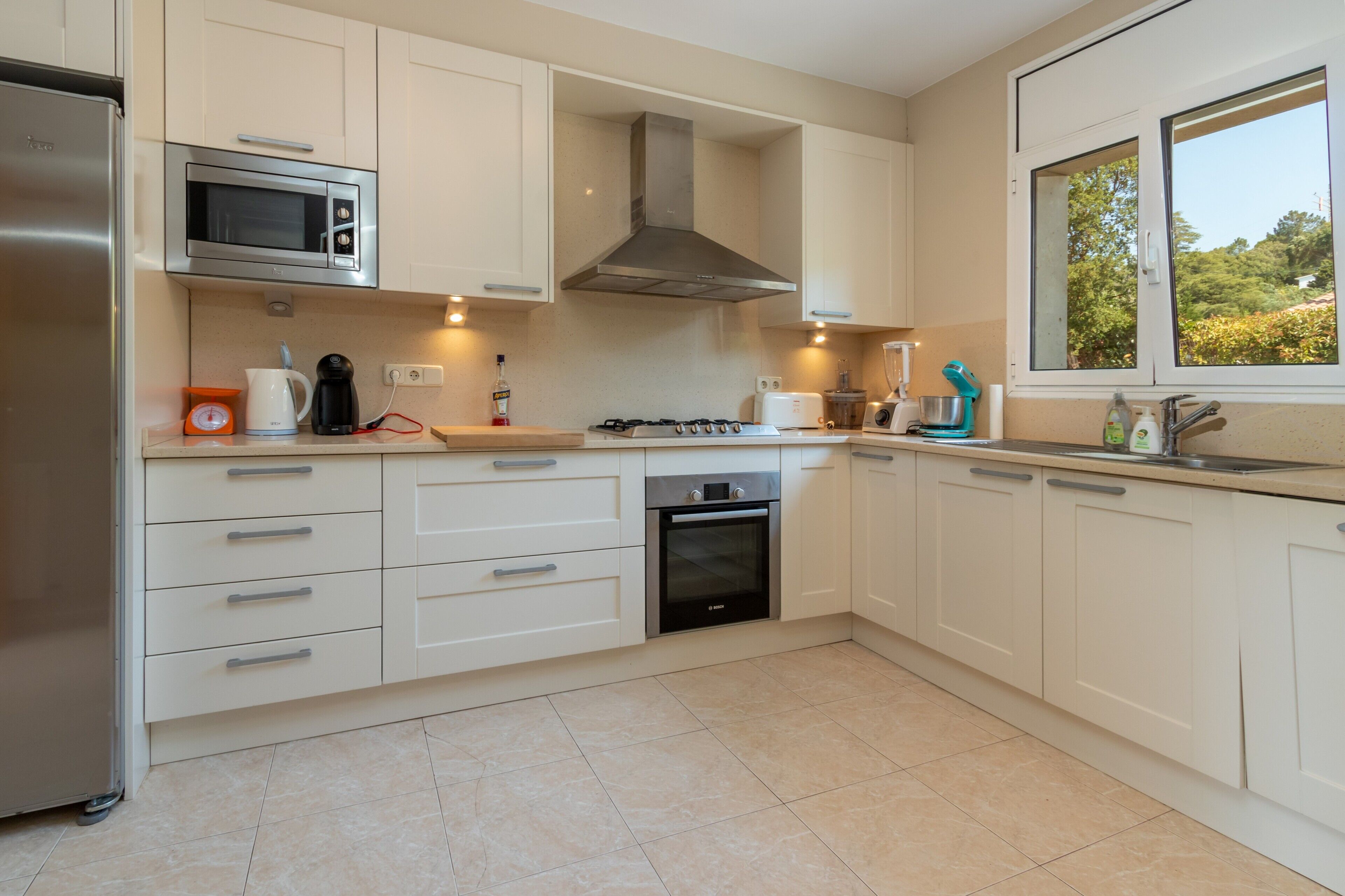 Una cocina moderna con refrigerador de acero inoxidable, microondas, estufa a gas, horno y ventana con vista a áreas verdes.