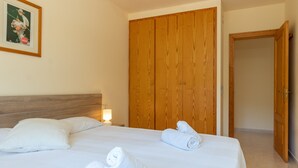 Hotellihuone, jossa on puinen vaatekaappi, valkoisilla lakanoiden peitetty sänky ja seinällä oleva kehystetty kuva.
