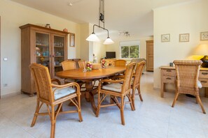 A dining area with a round table, wicker chairs, a cabinet with glass doors, and a window with a view.