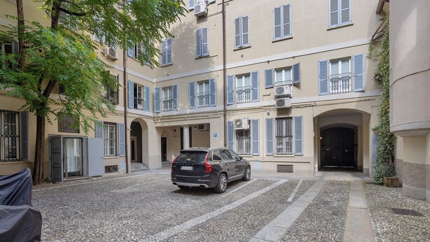 A courtyard with a parked car, stone pavement, and a building with multiple windows and balconies. - Apartment "Crocetta 10" in City Centre with Wi-Fi (Milano)