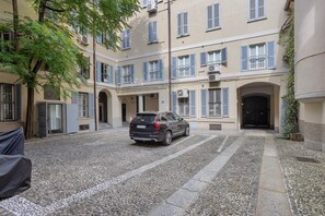 A courtyard with a parked car, stone pavement, and a building with multiple windows and balconies. - Apartment "Crocetta 10" in City Centre with Wi-Fi (Milano)