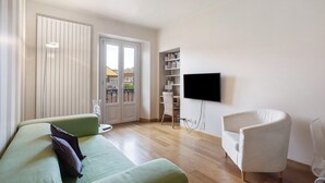A living room with a green sofa, a white armchair, a bookshelf, and a TV mounted on the wall. - Apartment "Crocetta 10" in City Centre with Wi-Fi (Milano)