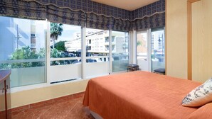 A bedroom with a large window, a bed with an orange bedspread, and a view of buildings and greenery outside. - Apartment 'Torre Del Mar' with Shared Pool, Shared Garden and Air Conditioning (Torre del Mar)