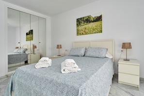 A bedroom with a bed, a nightstand, a lamp, a mirror, and a painting on the wall.